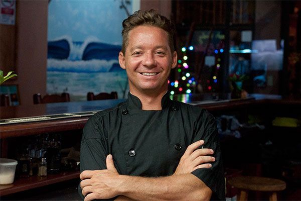 A man in a chef 's uniform is standing with his arms crossed and smiling.