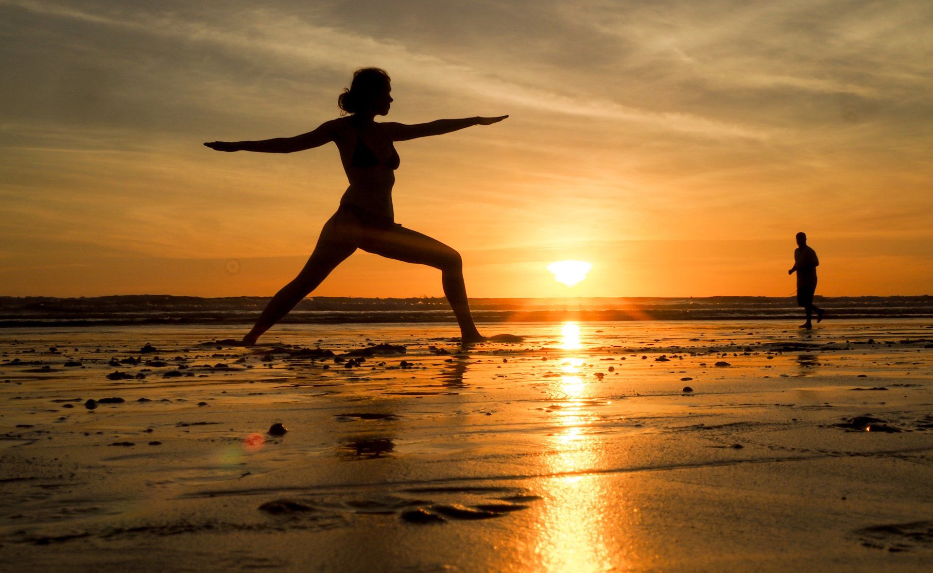 A woman is practicing yoga on the beach at sunset.