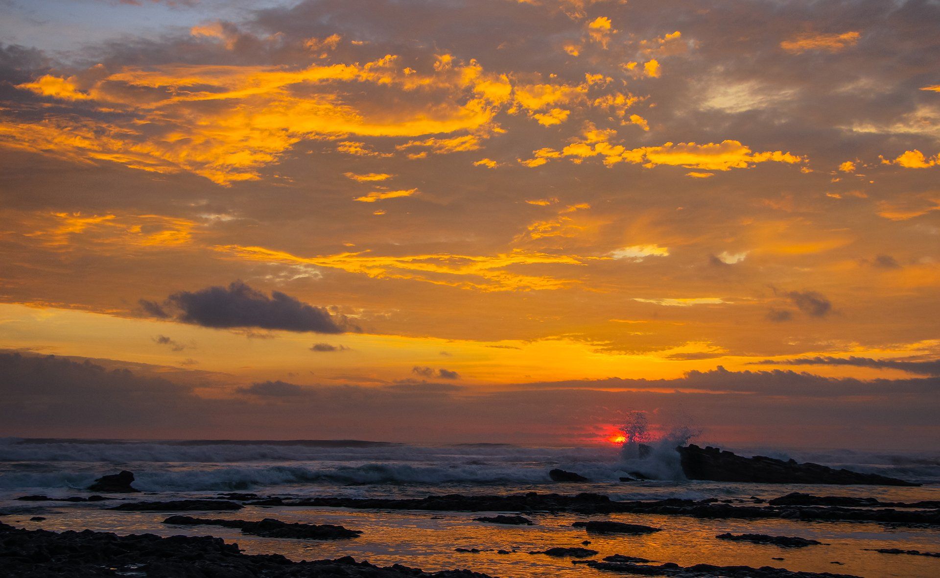 A sunset over the ocean with waves crashing on the shore.