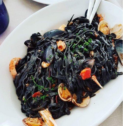 Pasta al nero di seppia con gamberi ed erbe aromatiche su un piatto bianco.