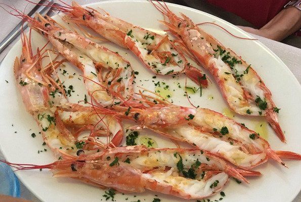 Piatto di gamberi cotti, guarniti con erbe aromatiche e salsa, serviti su un piatto bianco.