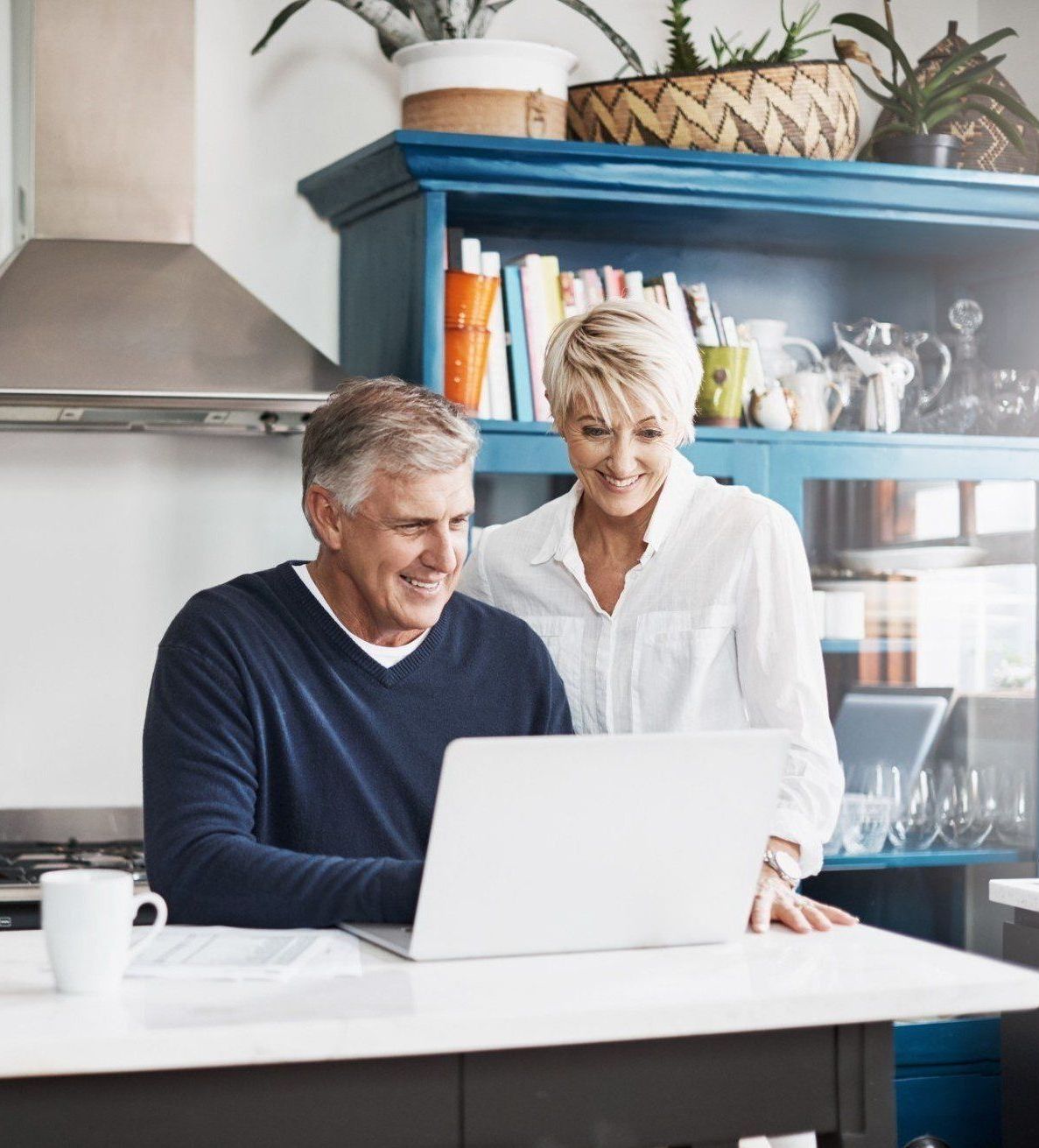A man and a woman are looking at a laptop in a kitchen.