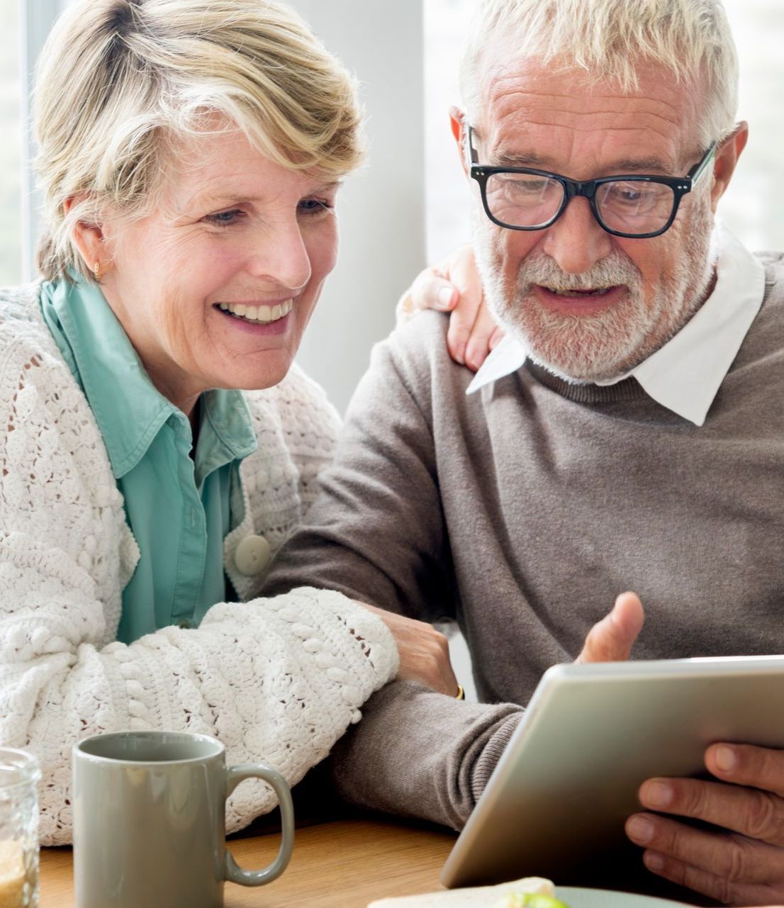 A man and a woman are sitting at a table looking at a tablet.
