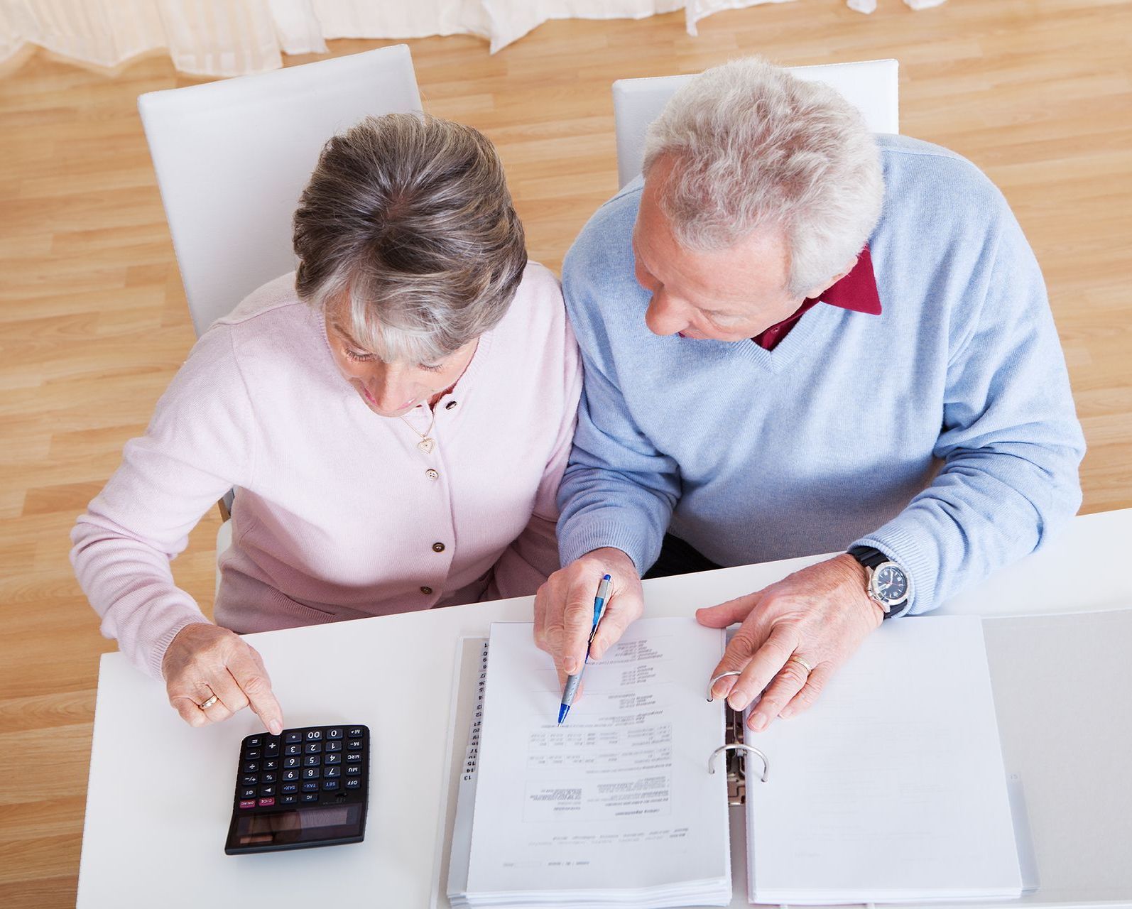 A man and a woman are sitting at a table looking at papers and a calculator.