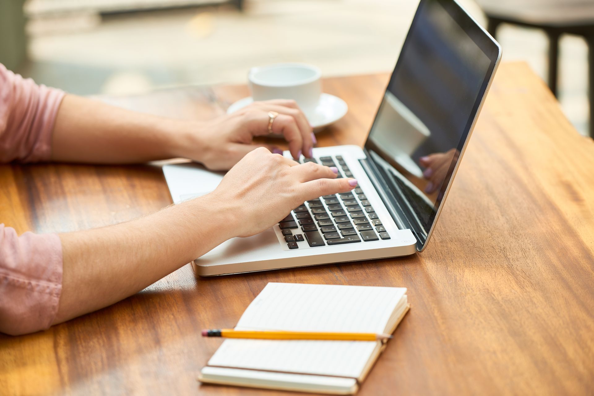A person is typing on a laptop computer at a wooden table.