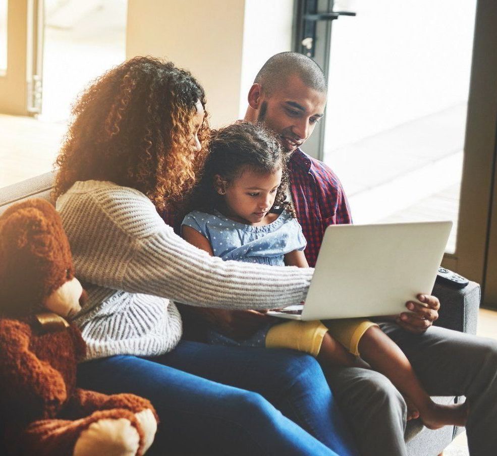 A family is sitting on a couch looking at a laptop.
