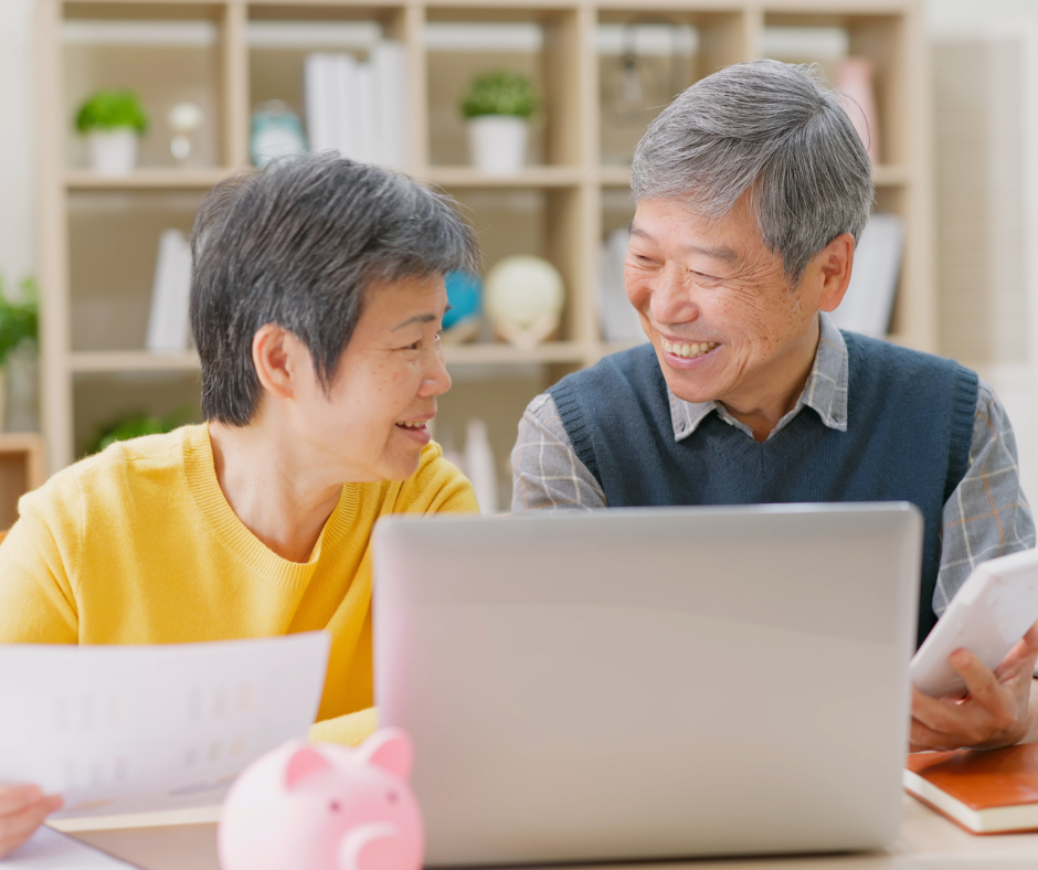 An elderly couple is sitting at a table looking at a laptop computer.
