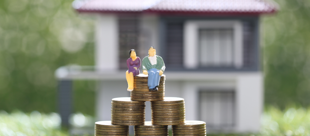 A couple of figurines sitting on top of a pile of coins in front of a house.