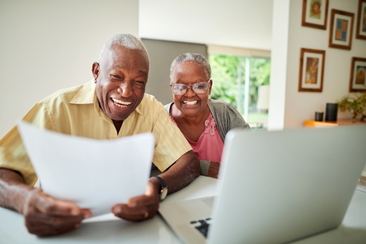 An elderly couple is smiling while looking at a laptop computer.