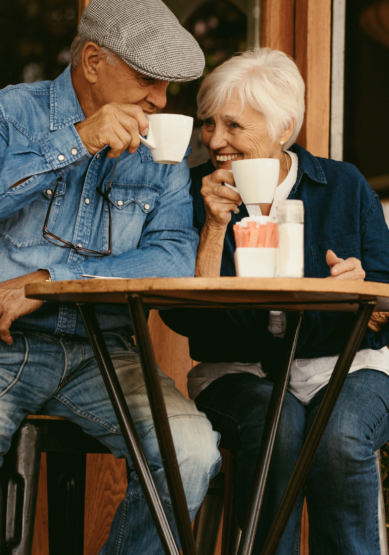 An elderly couple is sitting at a table drinking coffee.