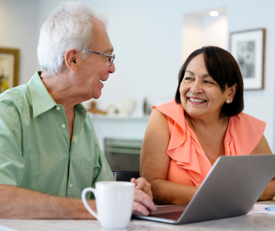 A man and a woman are sitting at a table looking at a laptop computer.