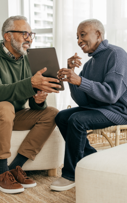 A man and a woman are sitting on a couch looking at a tablet.