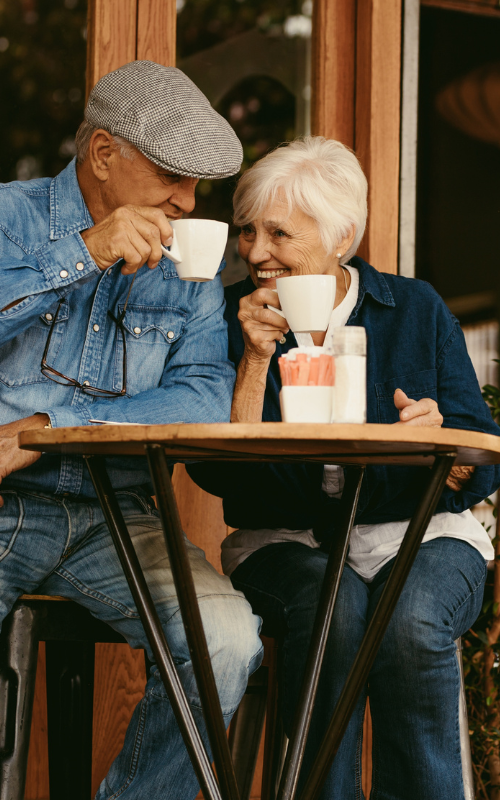 An elderly couple is sitting at a table drinking coffee.