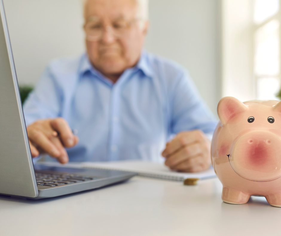 A man is typing on a laptop next to a piggy bank.