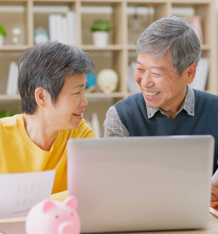 A man and a woman are sitting at a table looking at a laptop computer.