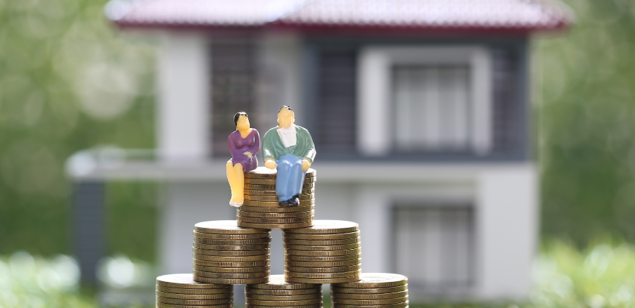 A couple of figurines sitting on top of a pile of coins in front of a house.