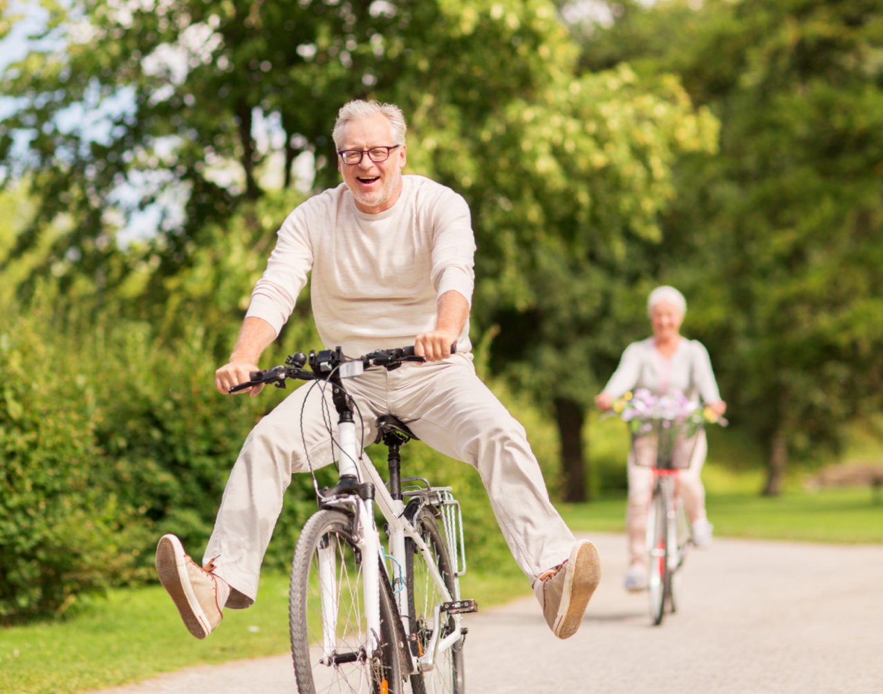 An elderly man is riding a bike with his legs in the air.