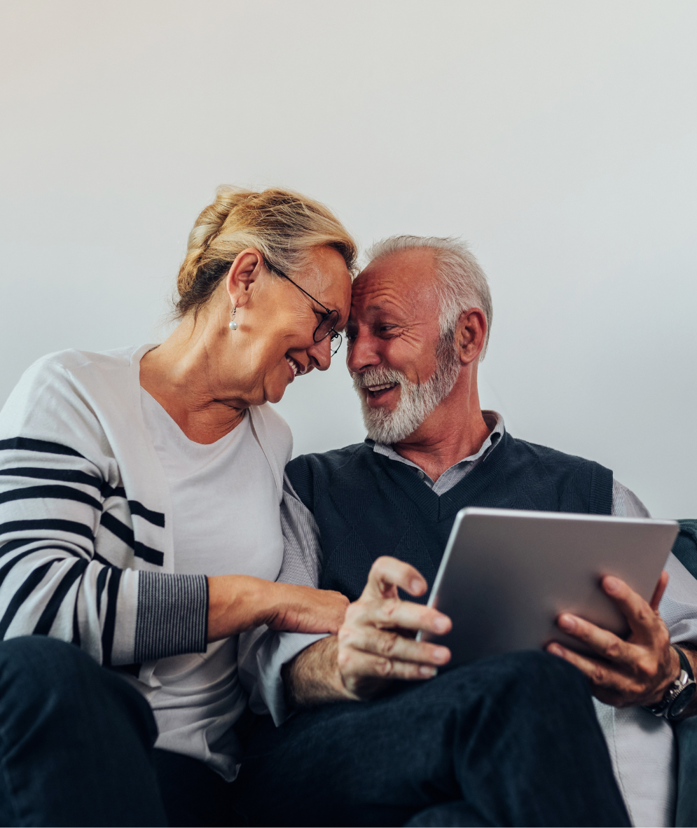 A man and a woman are sitting on a couch looking at a tablet.