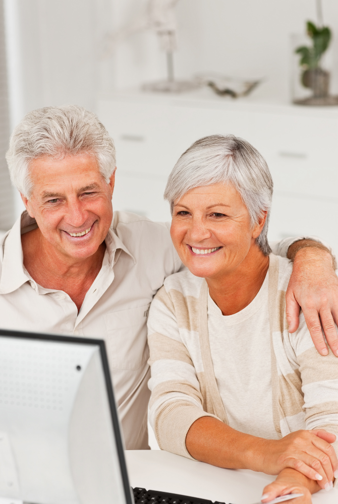 An elderly couple is smiling while looking at a laptop computer.
