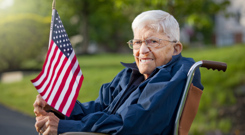 An elderly man in a wheelchair is holding an american flag.