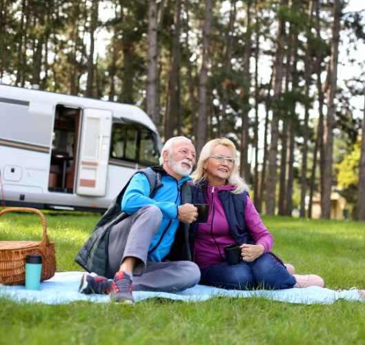 A man and a woman are sitting on a blanket in front of a camper van.