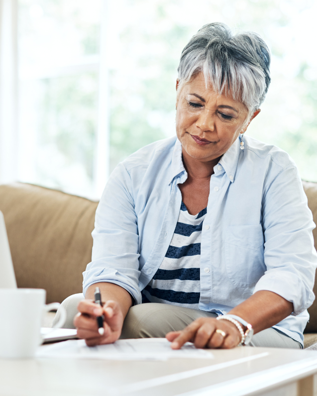 An older woman is sitting on a couch writing on a piece of paper.