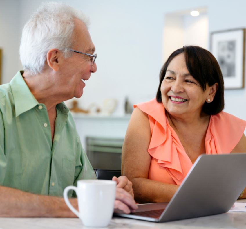 A man and a woman are sitting at a table looking at a laptop