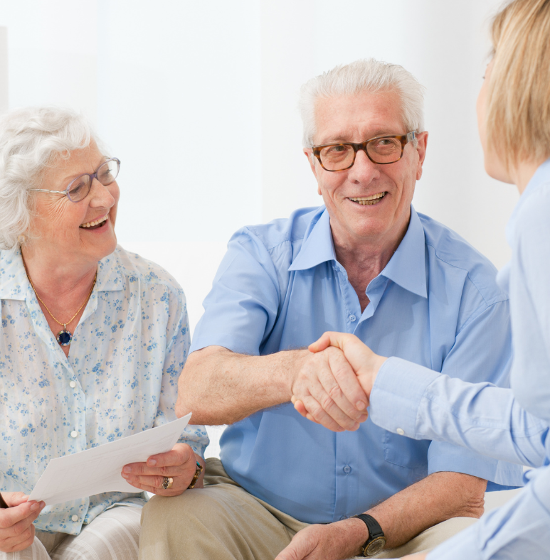 A man and woman shaking hands while a woman holds a piece of paper