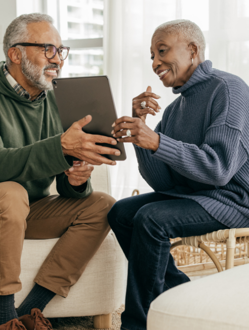 A man and a woman are sitting on a couch looking at a tablet.