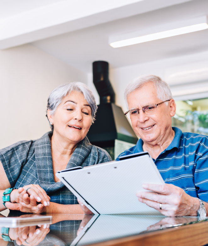 A man and a woman are sitting at a table looking at a tablet.