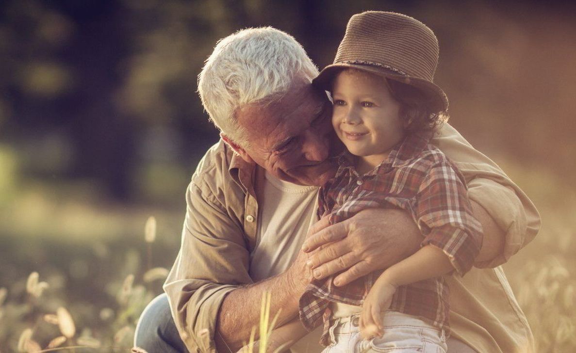 An elderly man is hugging a young boy in a field.