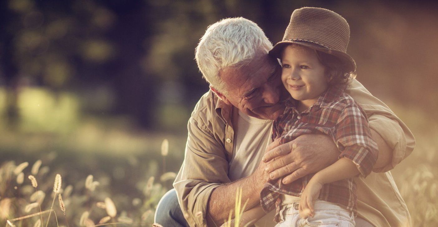 An elderly man is hugging a little boy in a field.