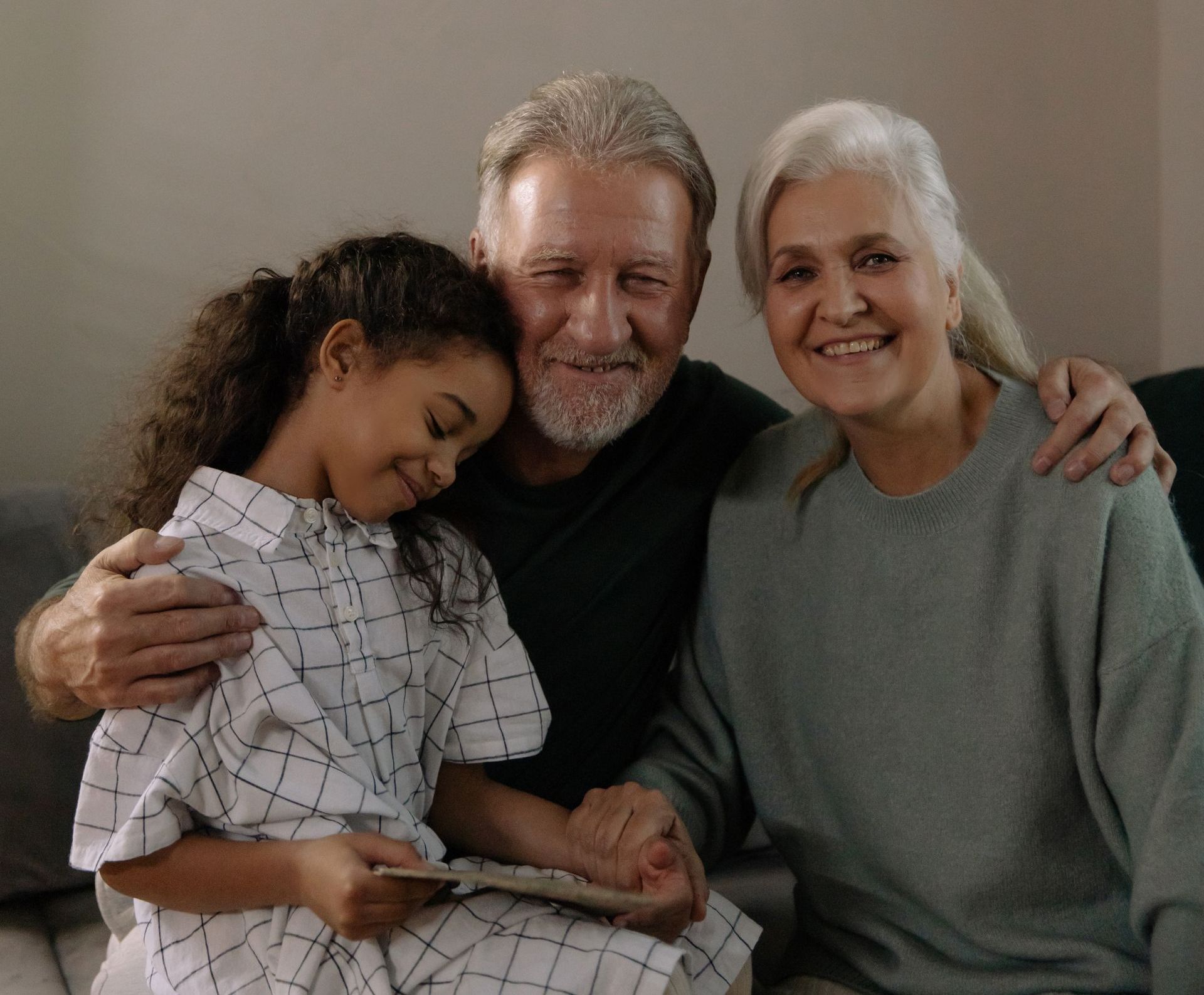 A little girl is sitting on a couch with her grandparents.