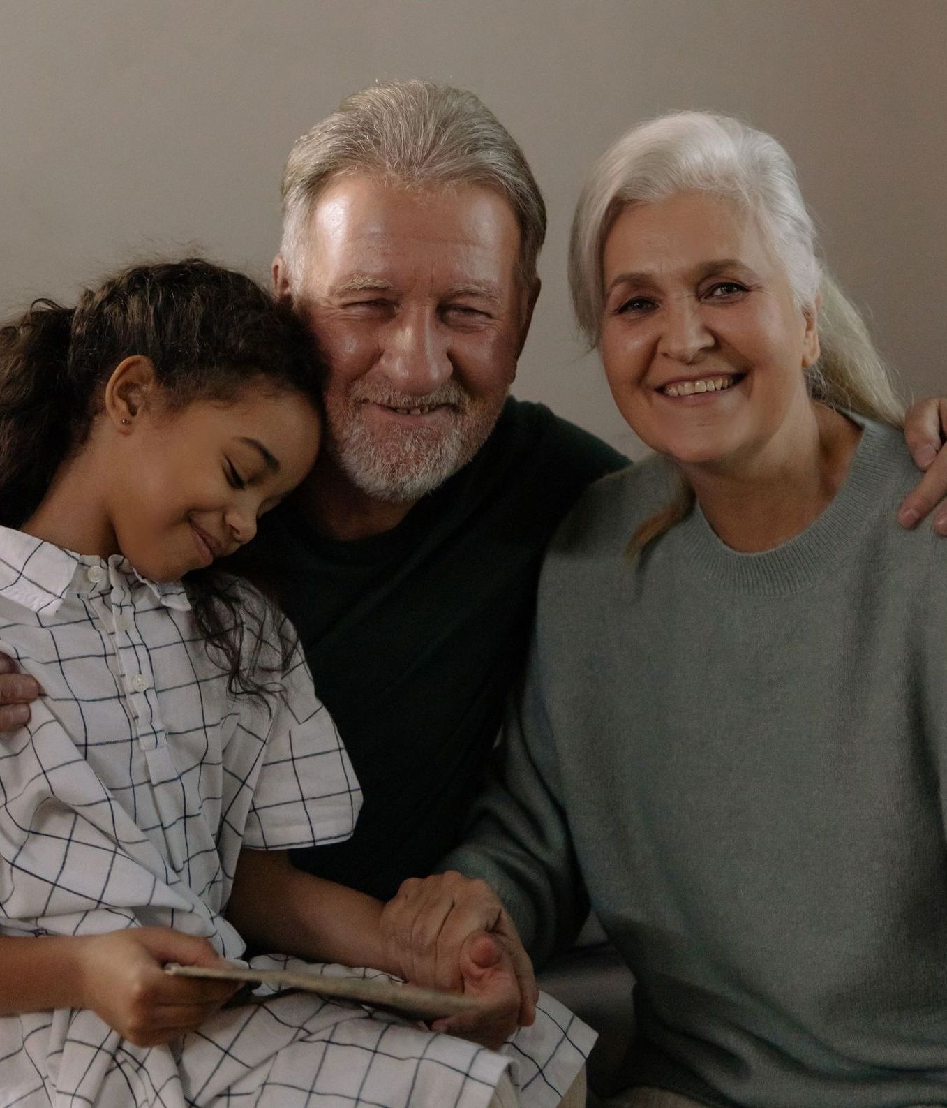 A man and woman are sitting next to a little girl who is holding a tablet.