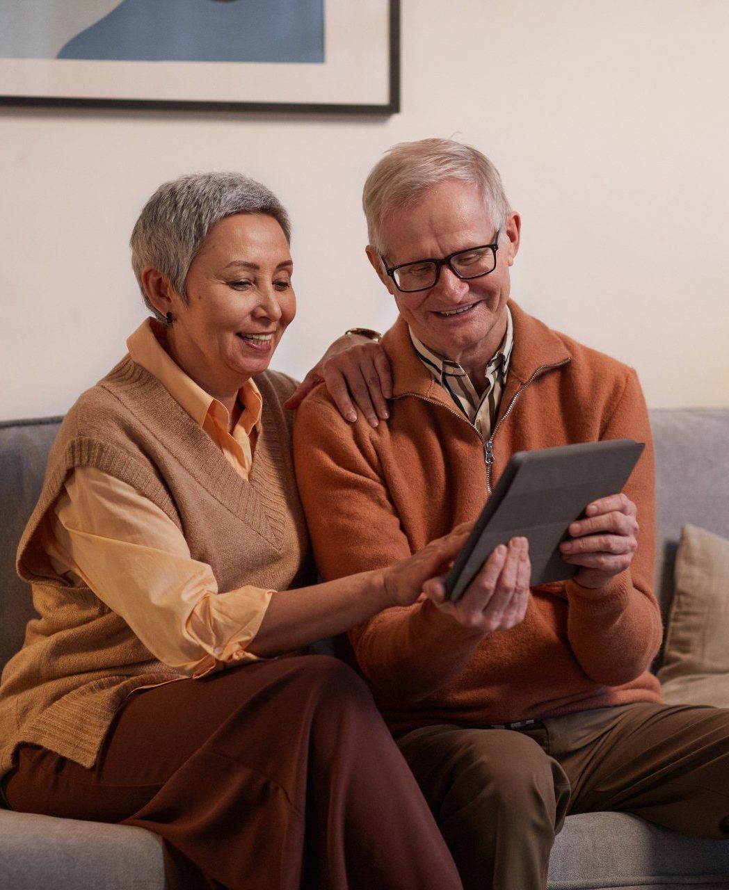 A man and a woman are sitting on a couch looking at a tablet