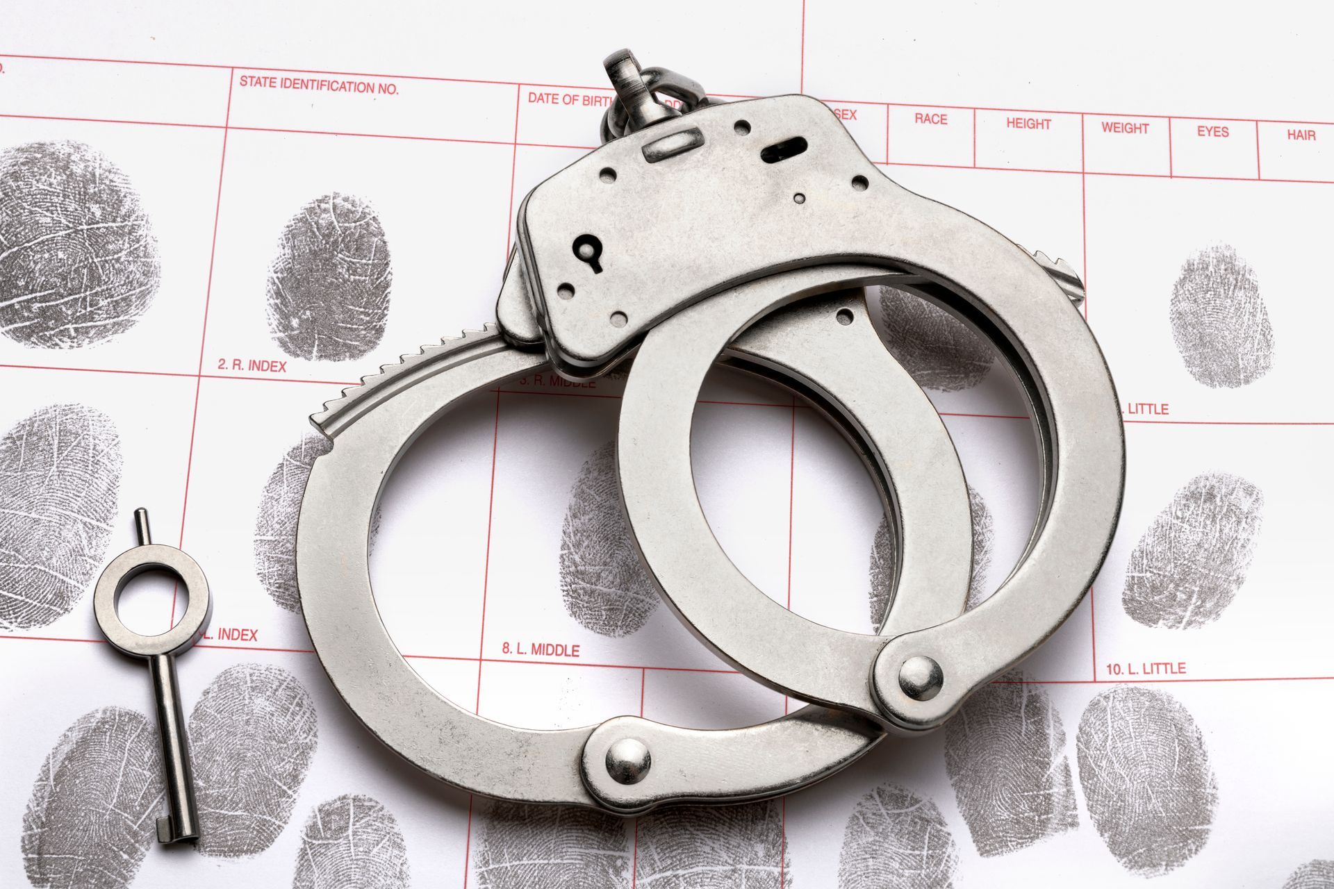 Silver handcuffs and key on fingerprint evidence sheet.