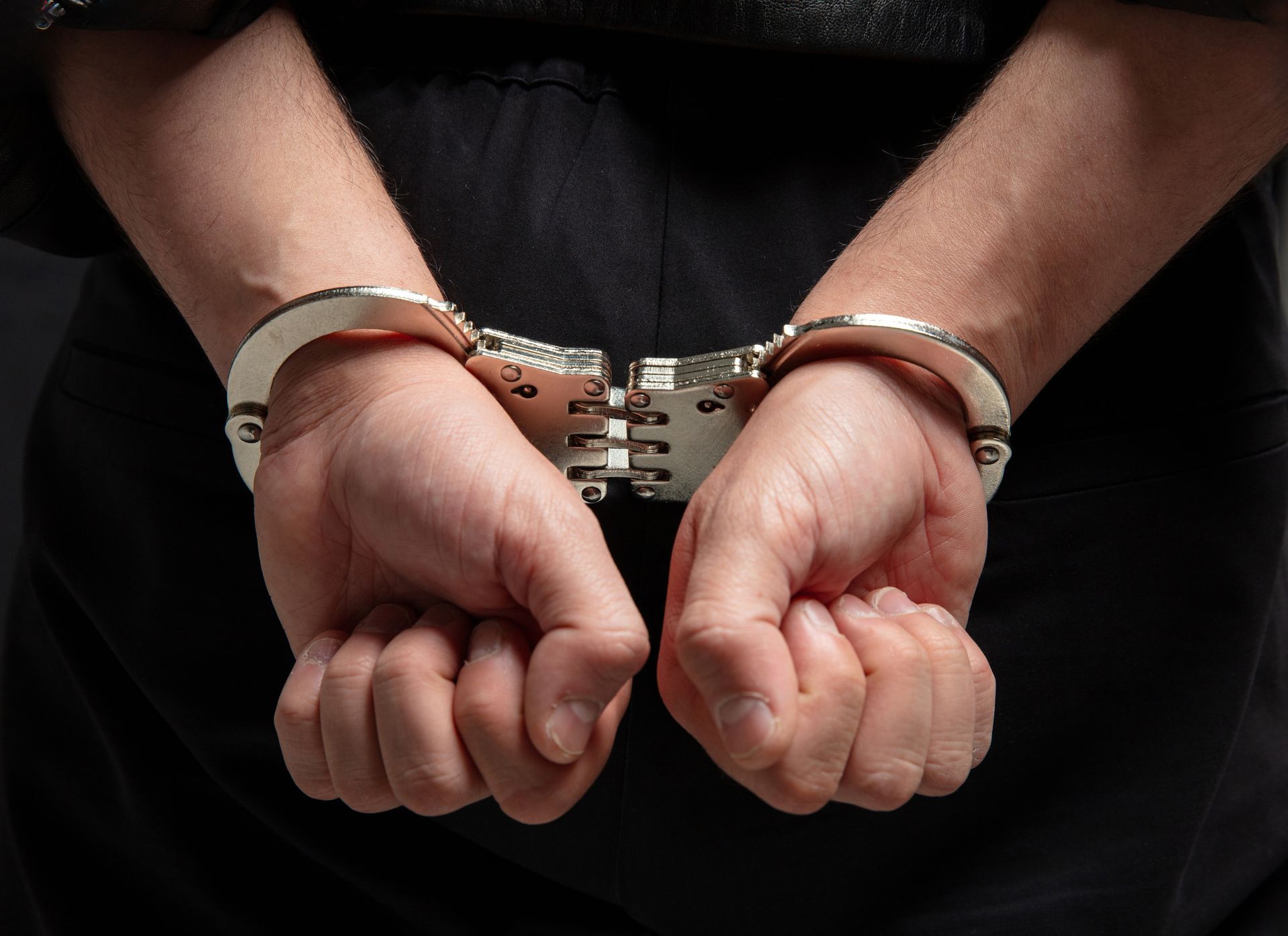 Handcuffed hands held behind the back against a dark background