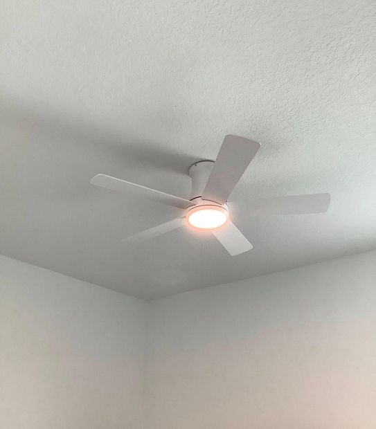 White ceiling fan with a light on in a plain white room corner
