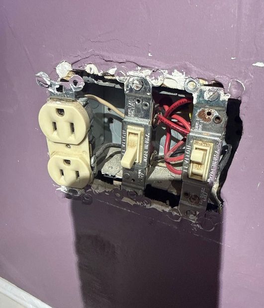Damaged wall outlet with exposed wires and a partially installed switch on a purple wall