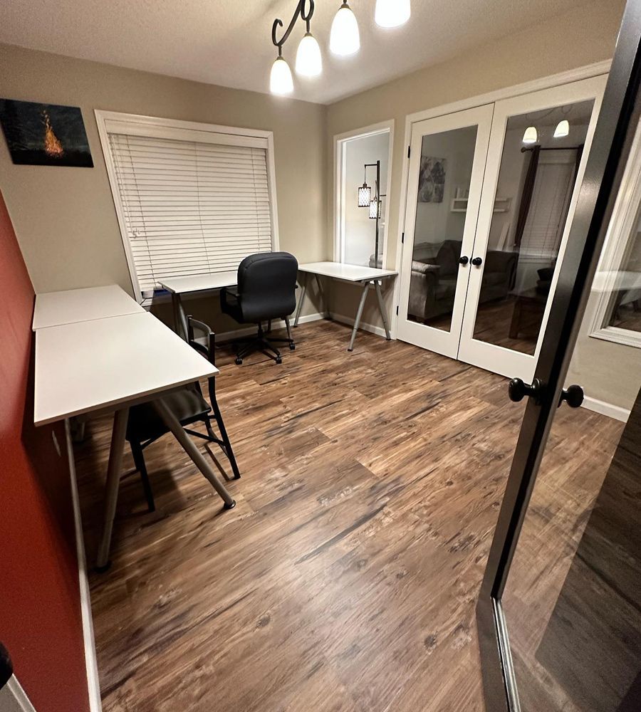 Home office with two white desks, black chair, wood floors, and French doors