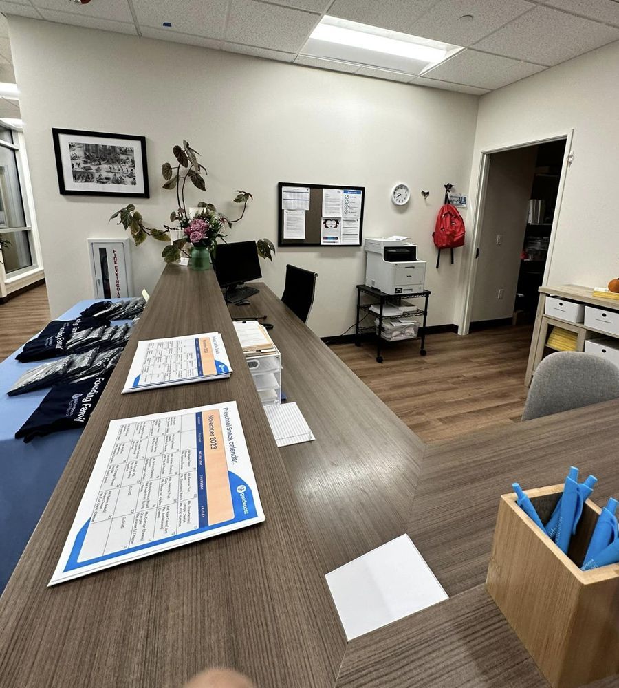Reception desk with brochures, flowers, wall art, a clock, and an office chair in a small lobby
