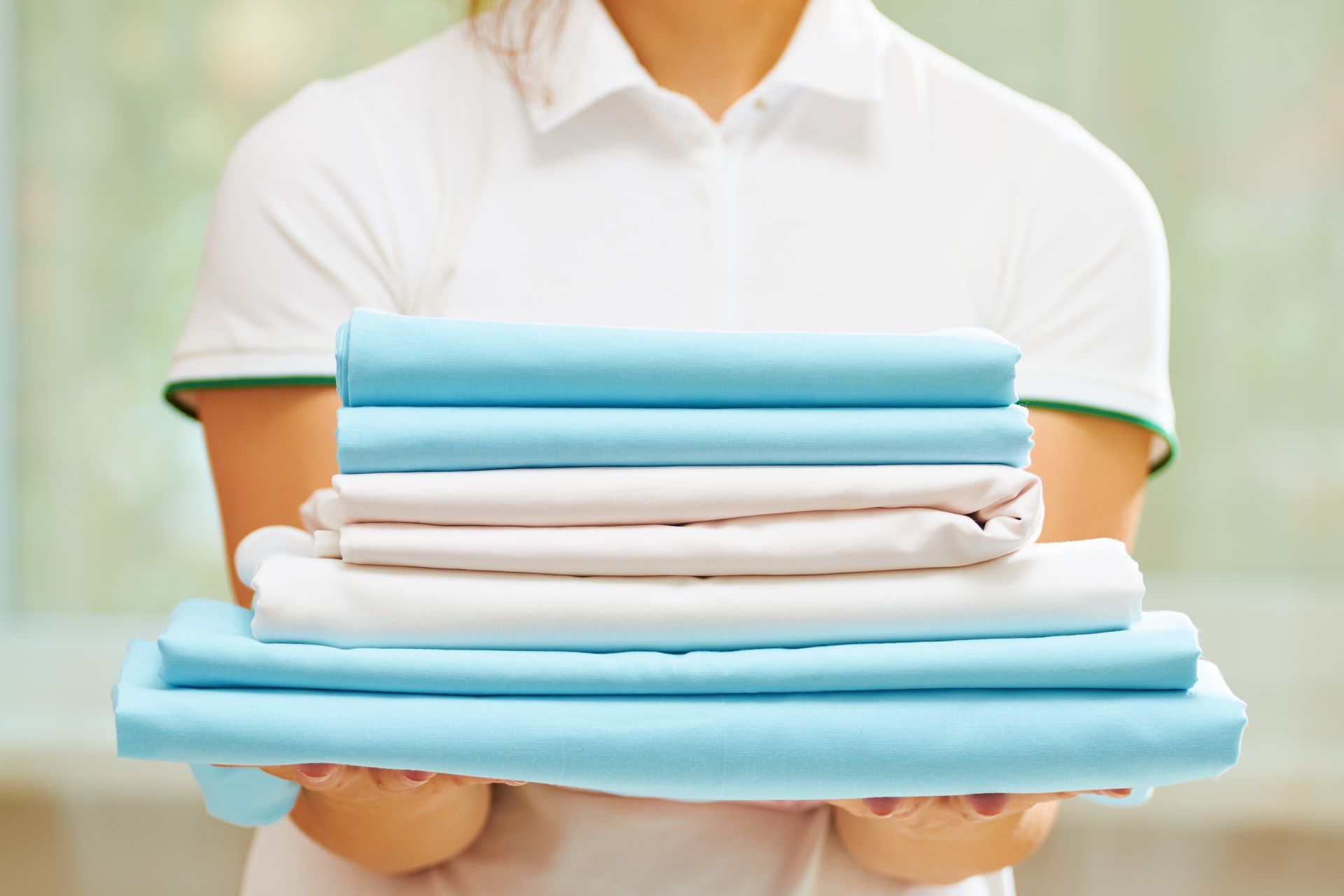 Person holding a stack of neatly folded pastel bed sheets.