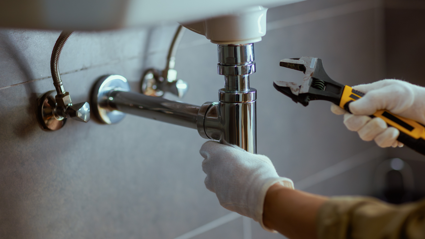 Gloved hands using pliers to repair a chrome pipe under a sink