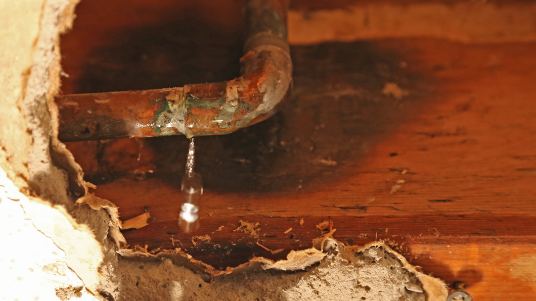 Rusty pipe leaking water over damaged wood and crumbling plaster