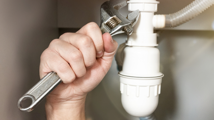 Hand tightening a wrench on a white sink drain pipe under a sink.