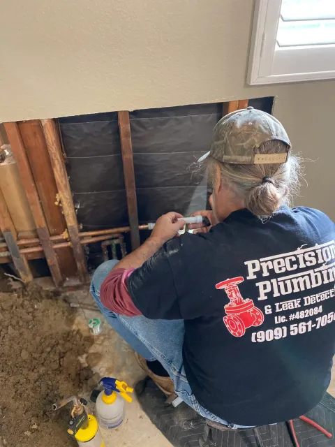Worker kneels in a wall cavity, inspecting insulation and wiring during home repair.