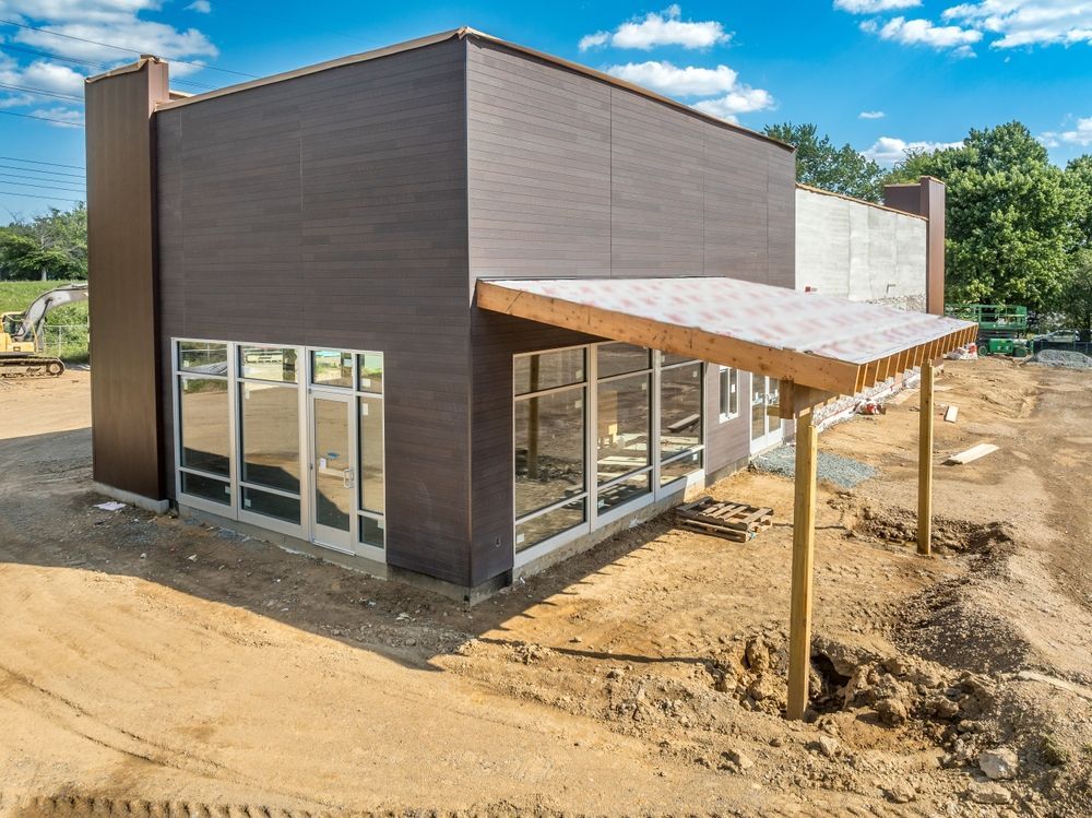 New dark brown building under construction with large windows and a covered porch
