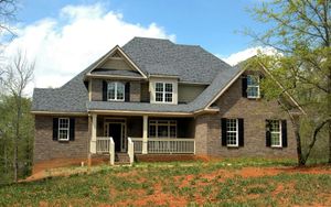 Brick house with dark roof and porch on a grassy hill.
