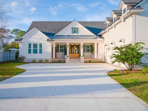 White house with a gray roof and long driveway.  Attached garage to the right. Green grass surrounds.