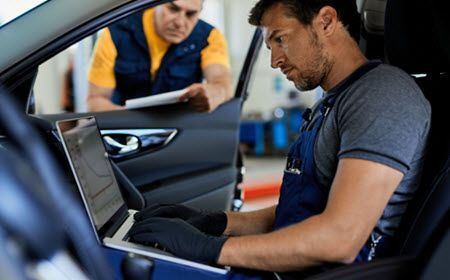 Man performing diagnostics inside car, another technician overseeing | Import Specialty Service